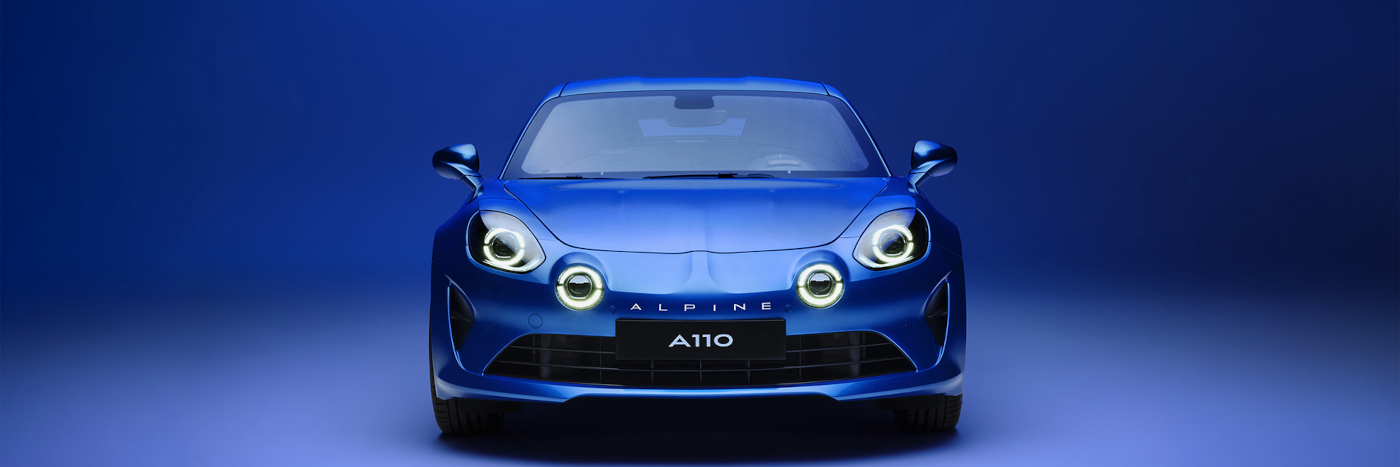 Alpine A110, sportliches blaues Auto mit hellen Scheinwerfern, vor einem blauen Hintergrund.